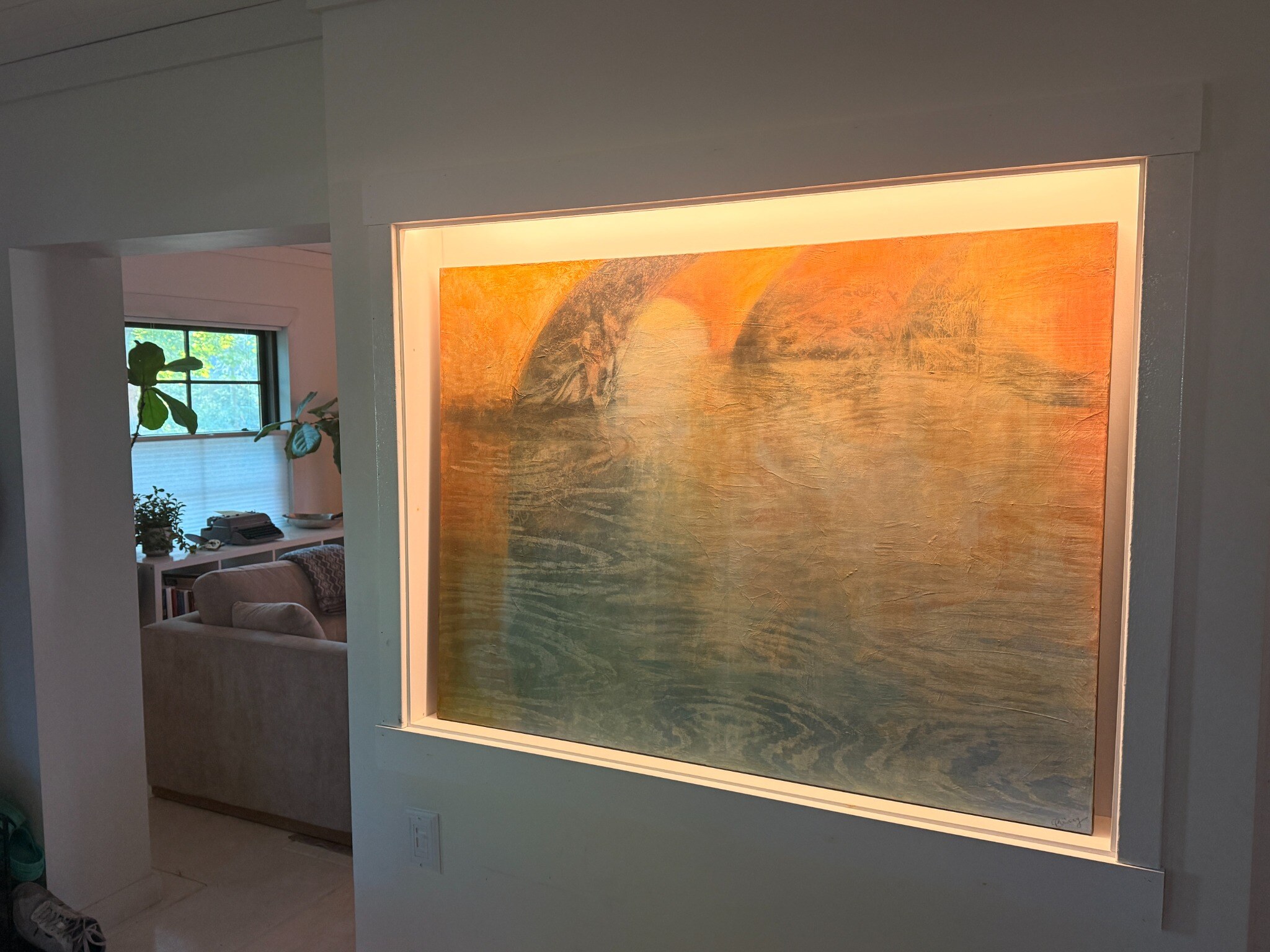 A large abstract painting fitted into a trim-framed wall niche and illuminated from above